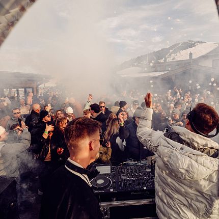 Menschenmenge bei einer Party im Freien mit DJ in den verschneiten Bergen.