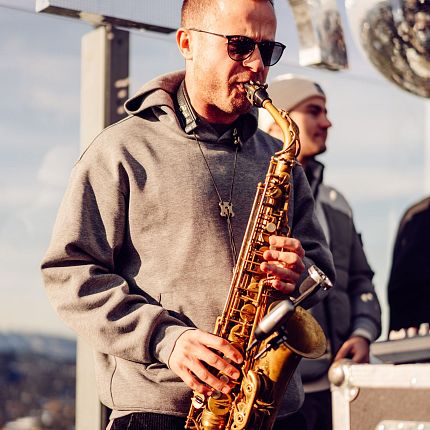 Straßenmusiker mit grauem Kapuzenpullover spielt Saxophon.