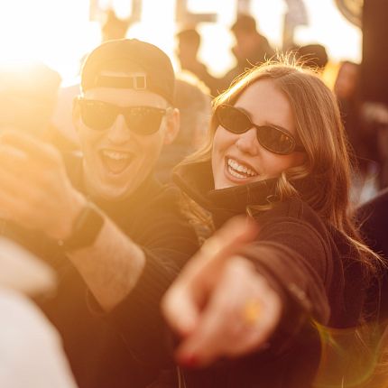 Two friends wearing sunglasses smiling outdoors in warm lighting.