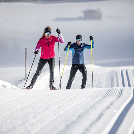 Zwei Langläufer auf einer verschneiten Loipe.