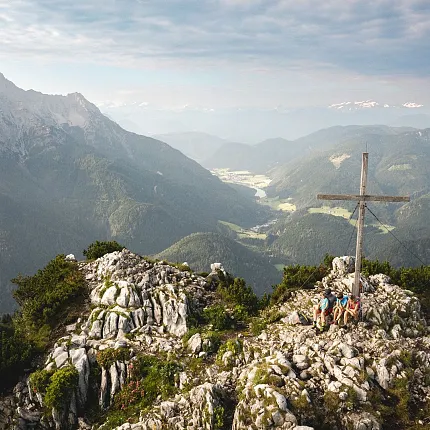 Wanderer auf einem Berggipfel mit Gipfelkreuz und Blick auf die Berglandschaft