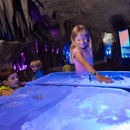 Kinder in einem interaktiven Museum mit blauen und violetten Lichtern.