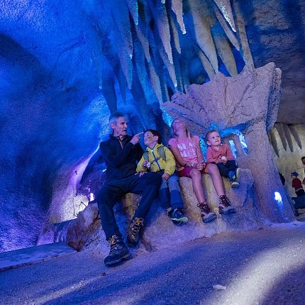 A family seated inside an ice cave with stalactites hanging above, bathed in blue light.