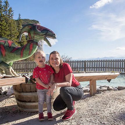 Woman and child posing in front of dinosaur sculpture at a park.