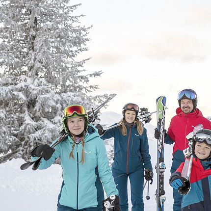 A family in ski gear posing in snow with ski equipment.