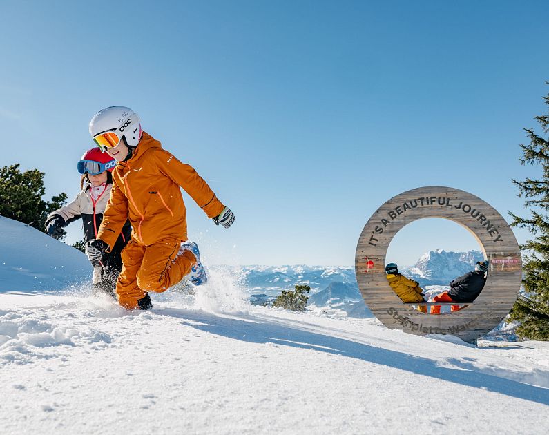 Kinder in Skibekleidung spielen im Schnee auf einem Berg.