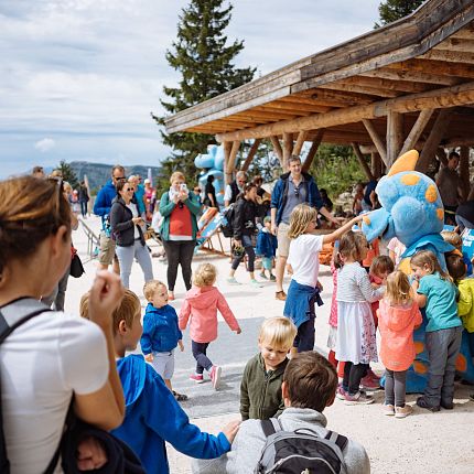 Children and parents at an outdoor event with a person in a colorful costume.