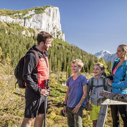 Family of four hiking in the mountains with a cliff in the background.