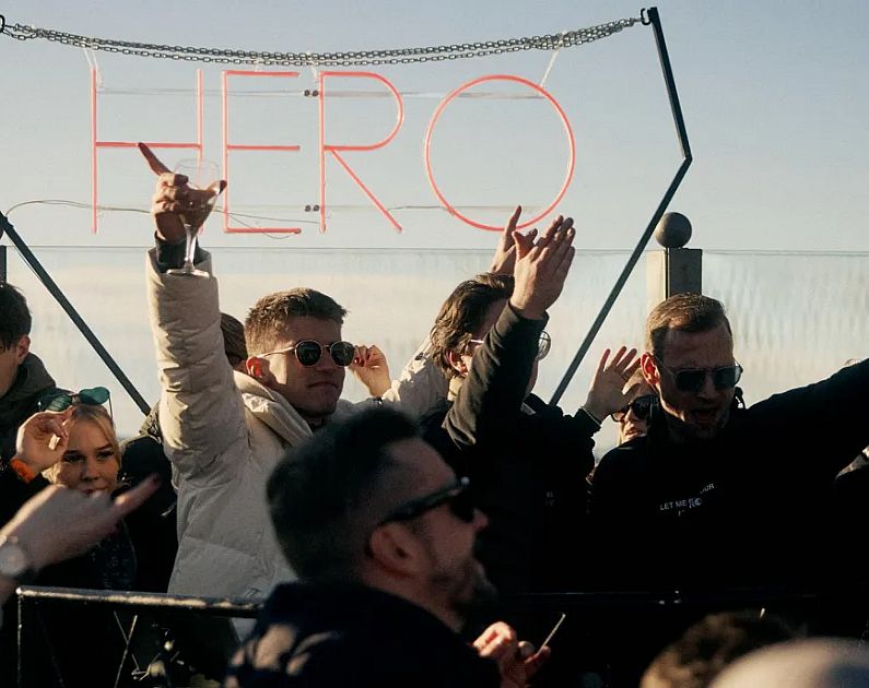 People celebrating on a snowy mountain with a 'HERO' sign above.