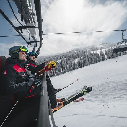 Skiers on a chairlift in a snowy mountain landscape.