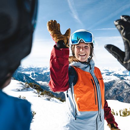 Person in Skikleidung gibt auf der Piste ein High Five.