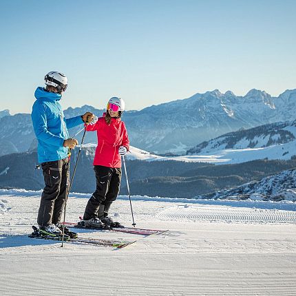 Two skiers on a snowy mountain slope with mountains in the background.