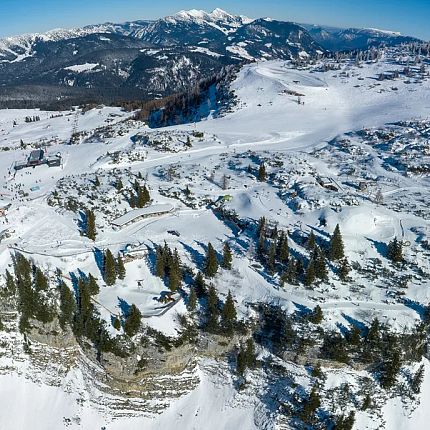 Luftaufnahme einer verschneiten Berglandschaft mit Bäumen und Gipfeln.