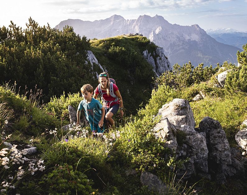 Two people hiking on a mountain trail with mountains in the background.